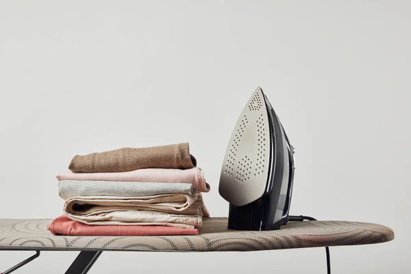 Iron and folded ironed clothes on ironing board isolated on grey — Stock Photo