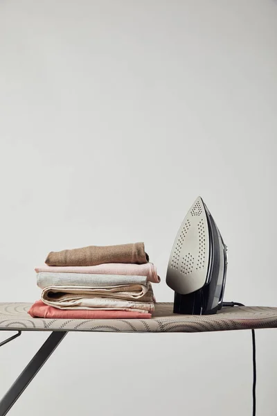 Bügeleisen und gefaltete gebügelte Kleidung auf Bügelbrett isoliert auf grau — Stockfoto