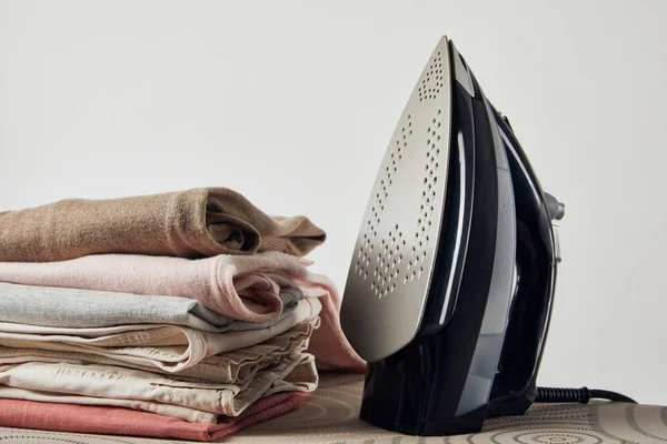 Iron and folded ironed clothes on ironing board isolated on grey — Stock Photo