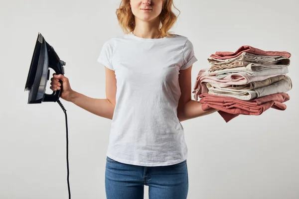 Femme partielle en t-shirt tenant du fer et des vêtements repassés pliés isolés sur gris — Photo de stock