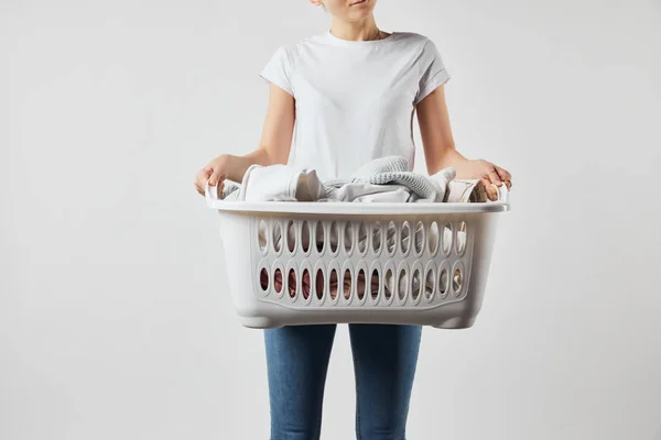 Cropped view of woman in jeans and t-shirt holding laundry basket with clothes isolated on grey — Stock Photo