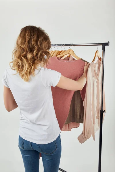 Back view of girl hanging hangers with clothes on straight rack on grey — Stock Photo