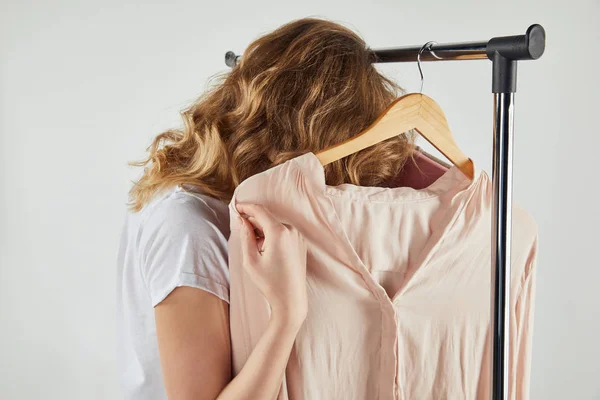 Back view of girl hanging hangers with clothes on straight rack on grey — Stock Photo