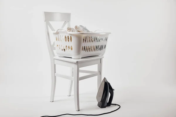 Chaise blanche, panier à linge avec vêtements et fer à repasser sur gris — Photo de stock