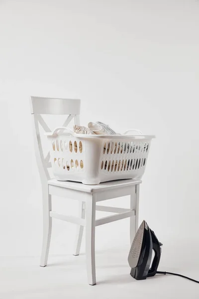 Chaise blanche, panier à linge avec vêtements et fer à repasser sur gris — Photo de stock