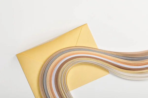 Yellow envelope with multicolored paper lines on grey background — Stock Photo