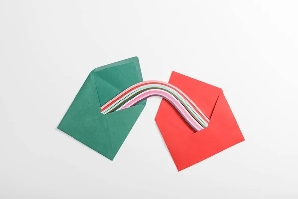 Вид сверху на зеленый и красный конверты с разноцветной радугой на сером фоне — стоковое фото