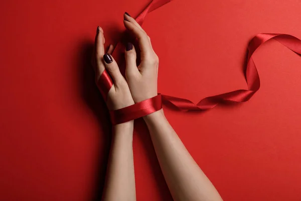 Partial view of woman tied with satin ribbon on red background — Stock Photo
