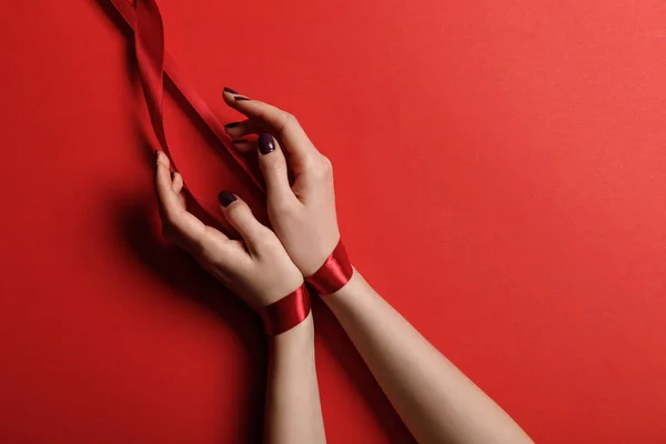 Cropped view of woman tied with silk ribbon on red background — Stock Photo