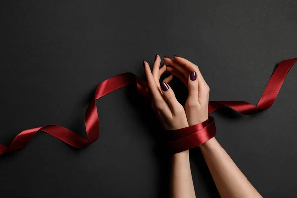 Cropped view of woman tied with silk red ribbon on black background — Stock Photo