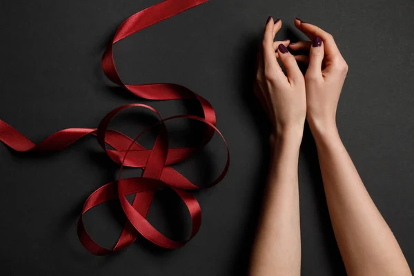 Cropped view of female hands near satin red ribbon on black background — Stock Photo