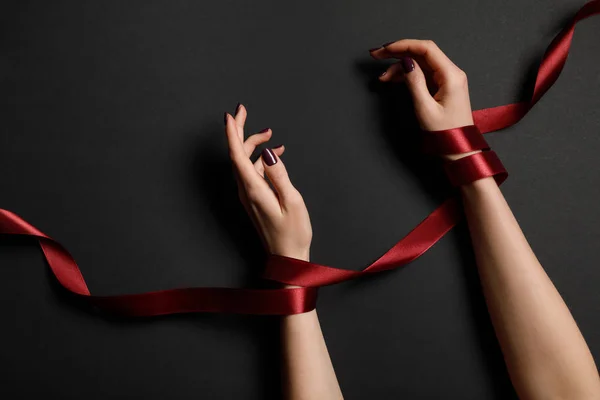 Partial view of female hands in red ribbon on black background — Stock Photo