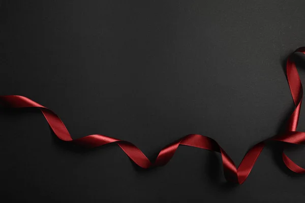 Top view of red silk wavy ribbon on black background with copy space — Stock Photo