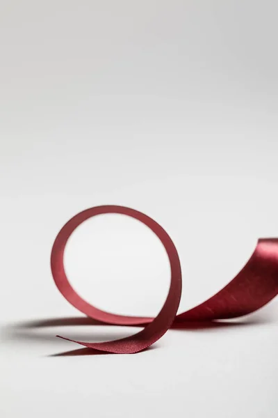 Satin curved burgundy ribbon on grey background — Stock Photo