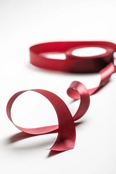 Selective focus of silk wavy burgundy ribbon with spool on grey background — Stock Photo