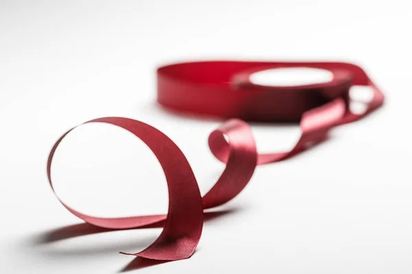 Selective focus of satin wavy burgundy ribbon with spool on grey background — Stock Photo