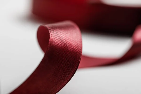 Selective focus of shiny silk curved burgundy ribbon on grey background — Stock Photo