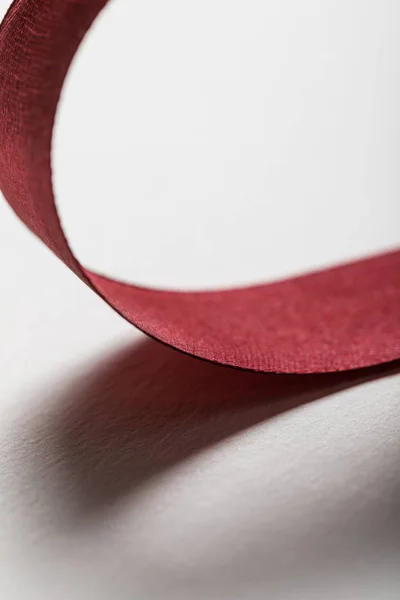 Close up of shiny silk wavy burgundy ribbon on grey background — Stock Photo