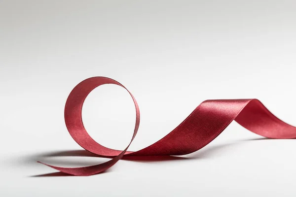 Shiny silk wavy burgundy ribbon on grey background — Stock Photo