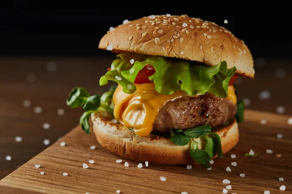 Close up of tasty meat burger with salt on wooden chopping board — Stock Photo