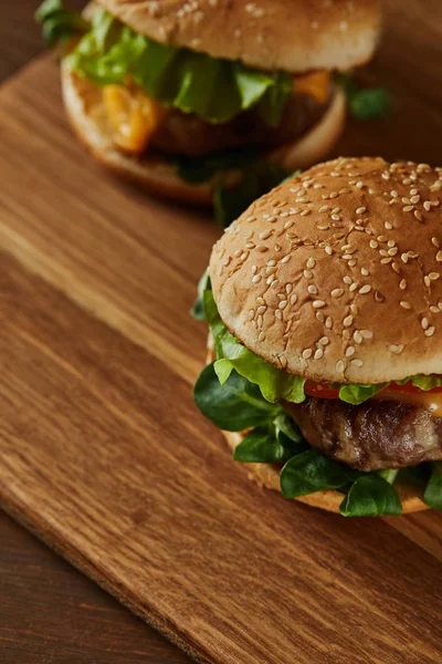 Selective focus of tasty meat burgers on wooden chopping board — Stock Photo
