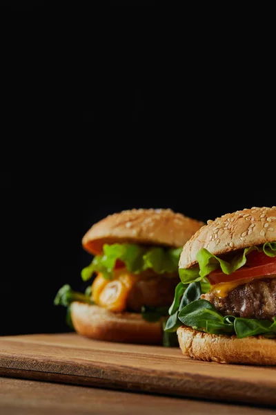 Selective focus of delicious meat burgers with cheese and sesame isolated on black — Stock Photo