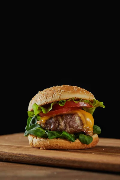 Delicioso hambúrguer de carne com queijo, vegetação e tomates e gergelim isolado em preto — Fotografia de Stock