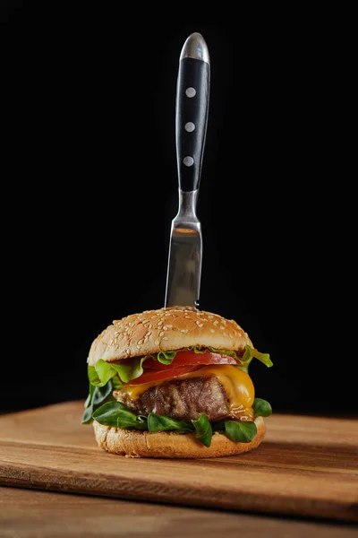 Messer im leckeren Fleisch-Burger mit Käse, Grün und Tomaten und Sesam isoliert auf schwarz — Stockfoto