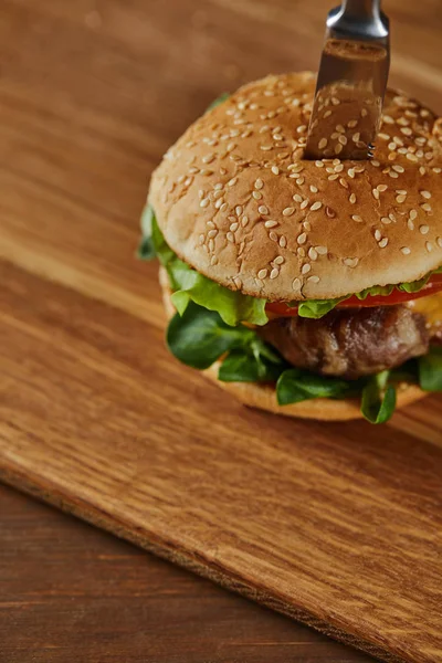 Knife in delicious meat burger with cheese, greenery and tomatoes and sesame — Stock Photo