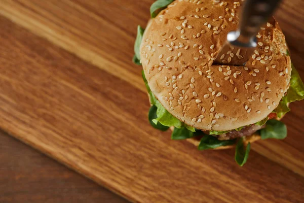 Foco seletivo de faca em delicioso hambúrguer em tábua de corte de madeira — Fotografia de Stock
