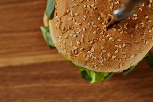 Vista superior del cuchillo en deliciosa hamburguesa sobre tabla de cortar de madera — Stock Photo