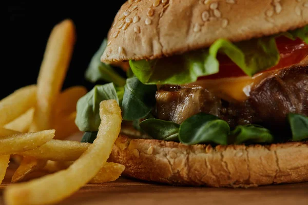 Close up de delicioso hambúrguer de carne com queijo, vegetação e gergelim perto de batatas fritas — Fotografia de Stock