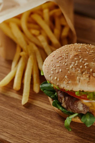 Selective focus of delicious burger with sesame on bun and french fries on wooden surface — Stock Photo