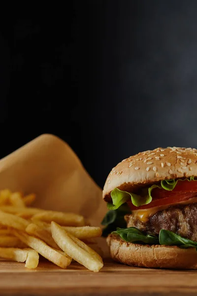 Foco seletivo de hambúrguer delicioso com carne e batatas fritas em fundo preto — Fotografia de Stock