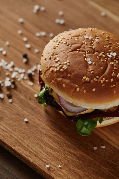 Delicious burger with salt and black pepper on wooden chopping board — Stock Photo