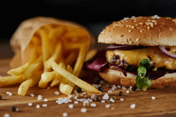 Fuoco selettivo di sale, patatine fritte e delizioso hamburger con carne sulla superficie di legno — Foto stock