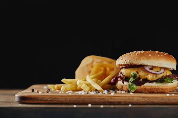 Salt and pepper, french fries and delicious burger with meat on wooden surface isolated on black — Stock Photo