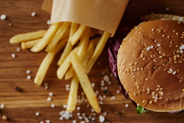 Blick von oben auf Salz, Pommes frites und leckeren Burger auf Holzoberfläche — Stockfoto