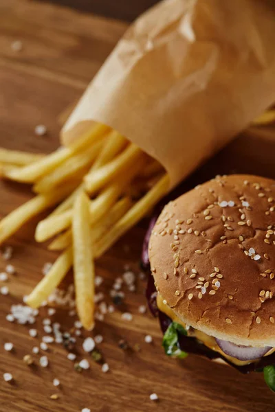 Foco seletivo de sal, batatas fritas e hambúrguer na superfície de madeira — Fotografia de Stock