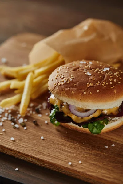 Enfoque selectivo de sal, pimienta, papas fritas y hamburguesa fresca en la superficie de madera — Stock Photo