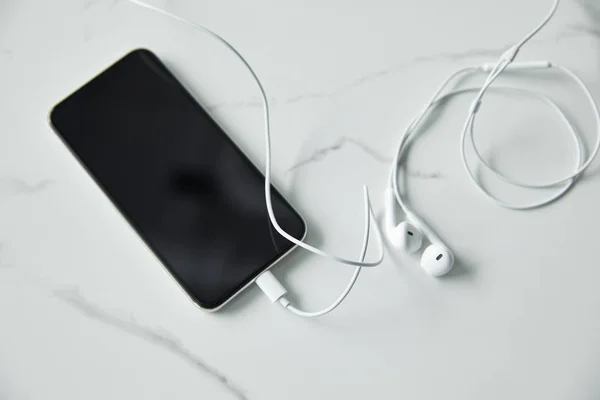 Top view of smartphone with blank screen and wired earphones on white marble surface — Stock Photo