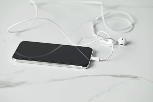 Selective focus of smartphone with connected earphones on white marble surface — Stock Photo