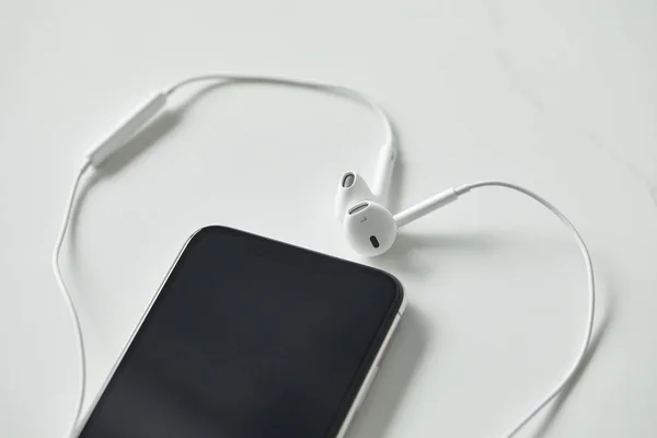 Enfoque selectivo del teléfono inteligente con pantalla en blanco y auriculares en la superficie blanca - foto de stock