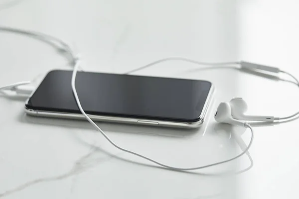 Foyer sélectif du smartphone avec écran vierge et écouteurs filaires sur surface blanche — Photo de stock