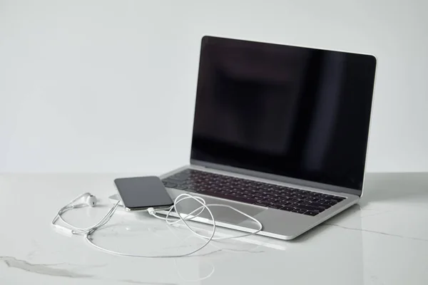 Laptop and smartphone with blank screen, and earphones isolated on grey — Stock Photo