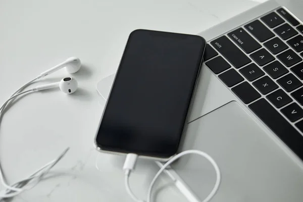 Laptop con teclado negro, smartphone con pantalla en blanco y auriculares en superficie blanca - foto de stock