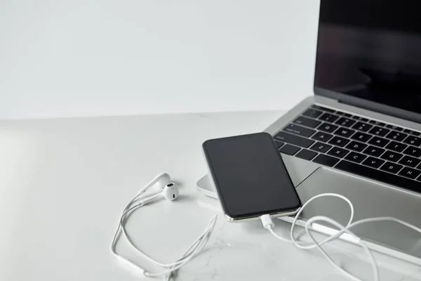 Laptop and smartphone with connected earphones isolated on grey — Stock Photo