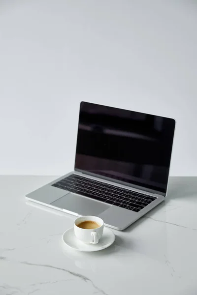 Laptop mit leerem Bildschirm und schwarzer Tastatur und Untertasse mit Kaffeetasse isoliert auf grau — Stockfoto