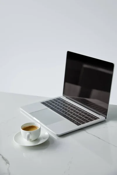 Enfoque selectivo de la computadora portátil con pantalla en blanco y taza de café aislado en gris - foto de stock