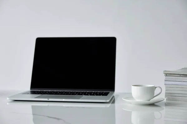 Ordinateur portable avec écran blanc, pile de journaux et tasse de café isolé sur gris — Photo de stock